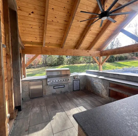 High-end custom outdoor kitchens showcasing a natural stone veneer base, a wood-fired pizza oven, and luxury granite countertops for alfresco dining.